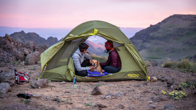 Two women sit in tent with their dog at sunset.