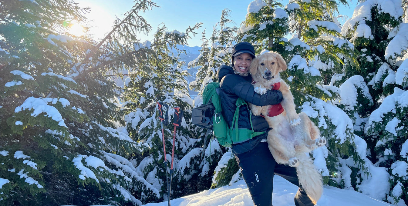 A woman picks up her golden retriever dog and poses with him in the snow. 