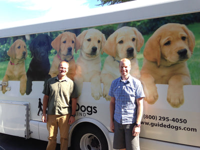 Two Ruffwear employees stand in front of a Guide Dogs for the Blind bus. 