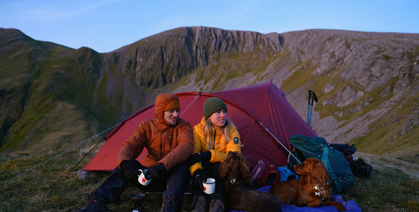Man and woman sitting in front of tent next to two dogs