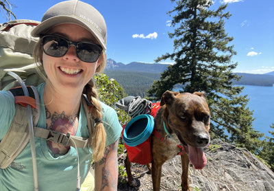 A woman goes backpacking in the mountains with her dog. 