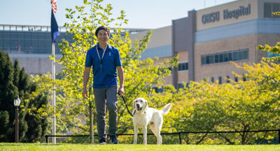 A man and his dog stand on the grass in front of OHSU Hospital.