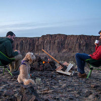 Cory and Rafa sit with dog Bondi by a campfire near a canyon.